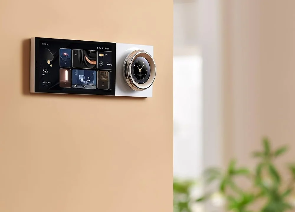 A wide smart screen with a round clock dial mounted on a warm beige wall